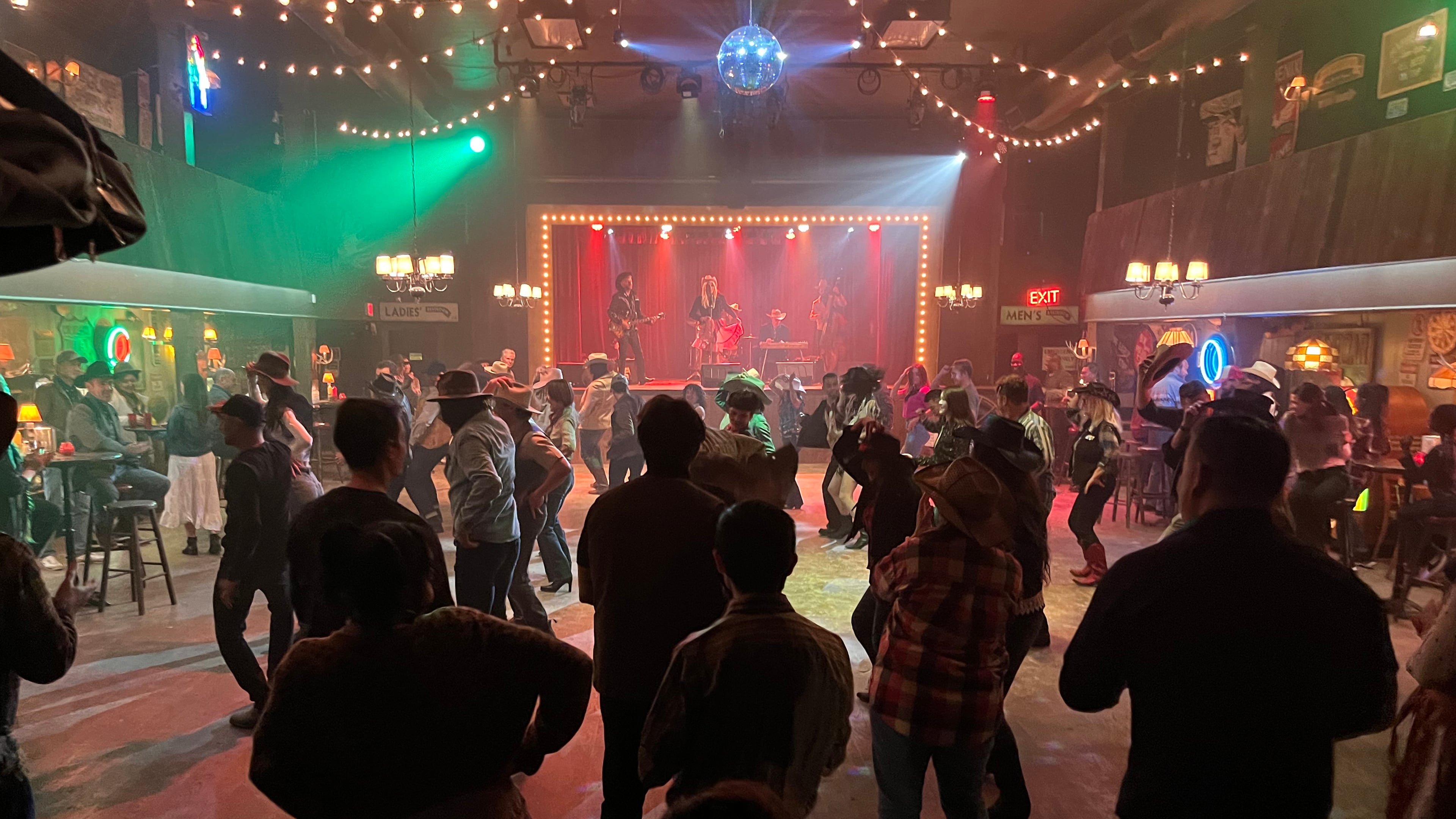 Crowd dancing on the honkytonk floor with live band on stage under colored lights for Expedia commercial