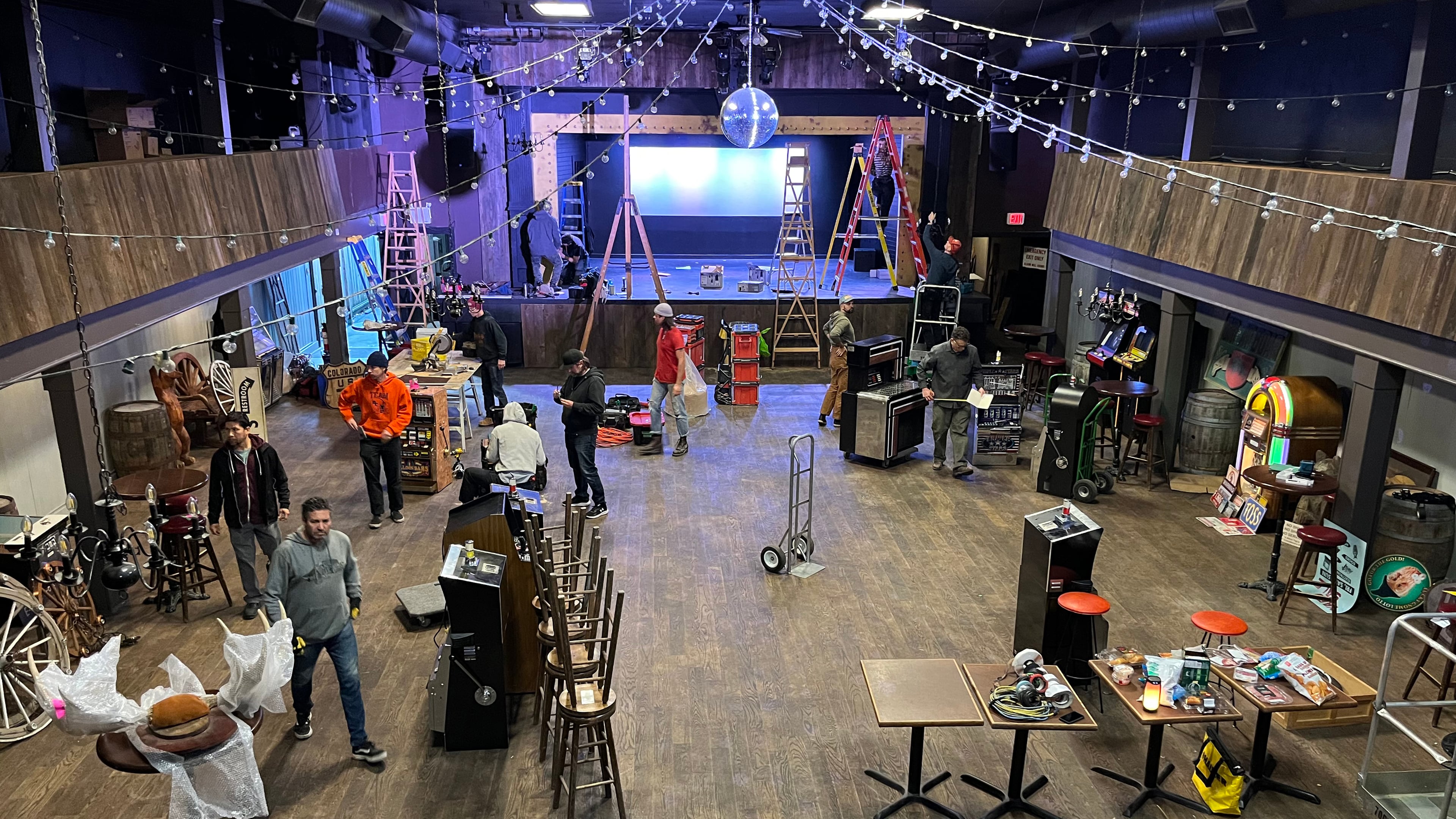 Crew setting up the honkytonk bar set with ladders, props, and equipment on the construction floor for Expedia commercial