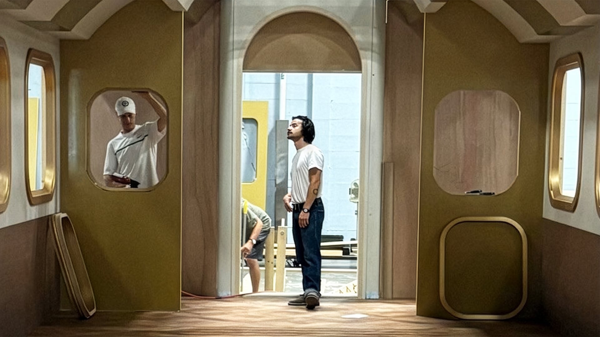 Crew member standing in doorway of train cabin set inspecting gold-trimmed interior with oval windows for MGM Grand