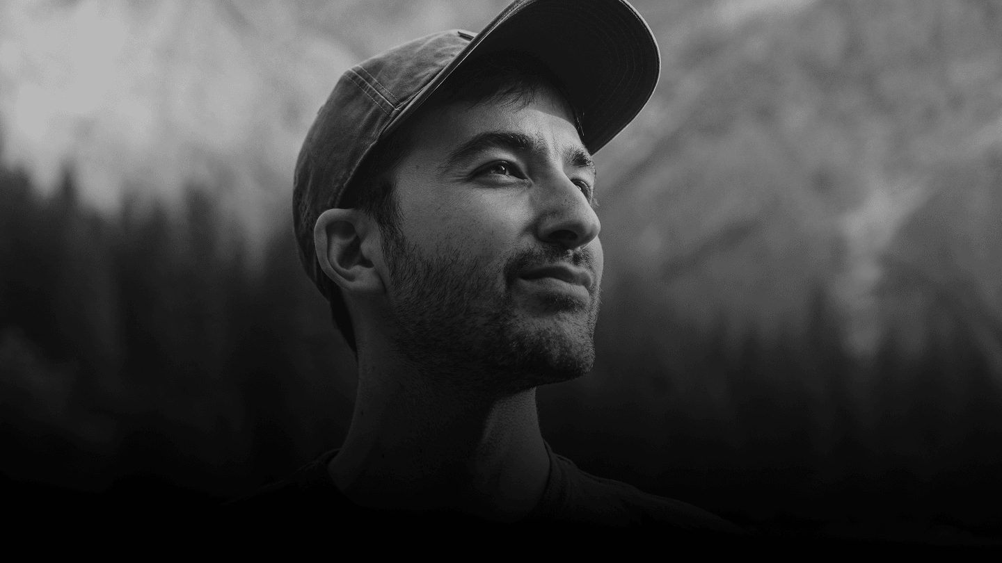 Black and white portrait of bearded man in baseball cap gazing upward against blurred forest background